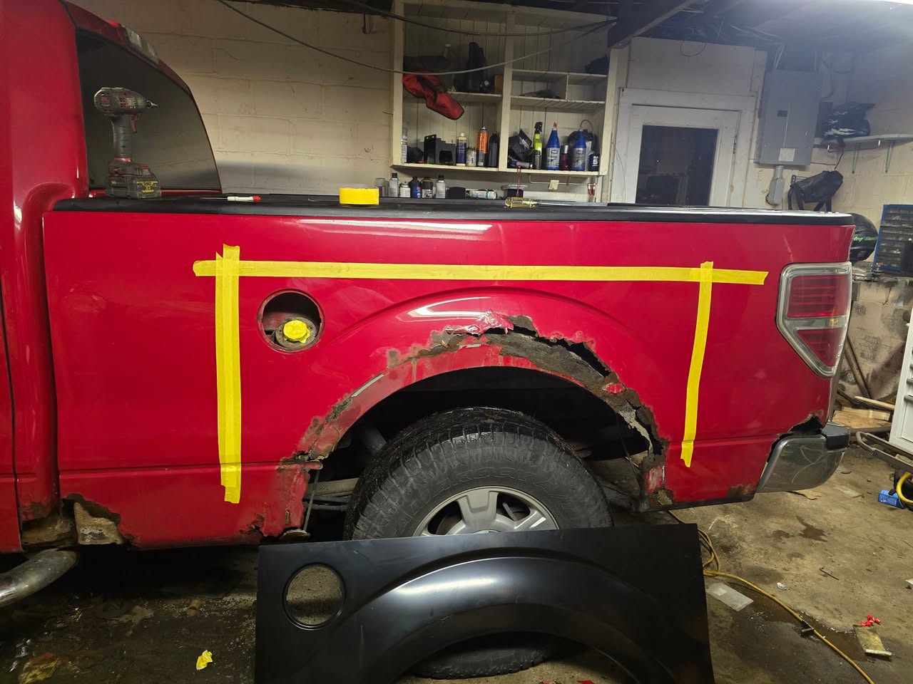 Rust damage around the rear wheel opening of a red pickup before repair